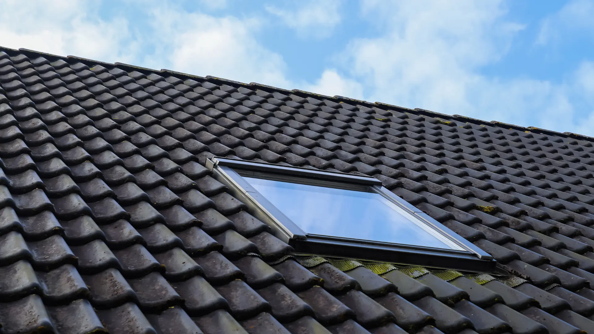 Roof window fitted flush into a grey tiled pitched roof